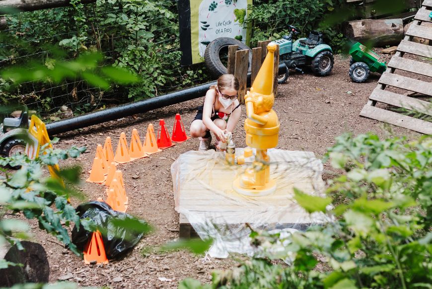 a girl spray painting a norbot sculpture gold outdoors